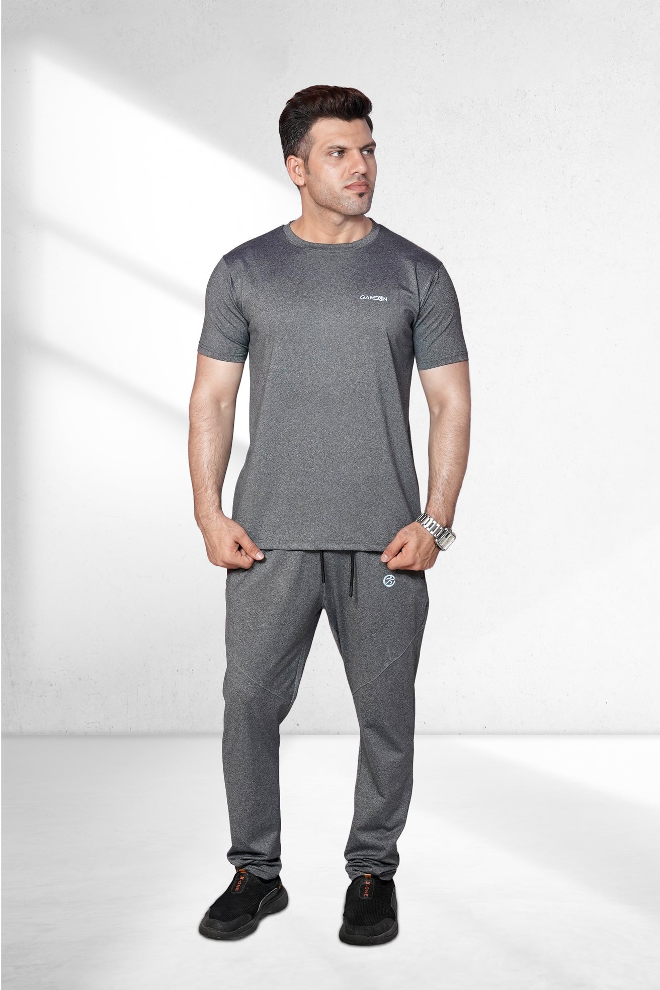 A person wearing a sleek gray track suit, running on a city street at dusk. The fabric looks lightweight and the fit is modern and streamlined.